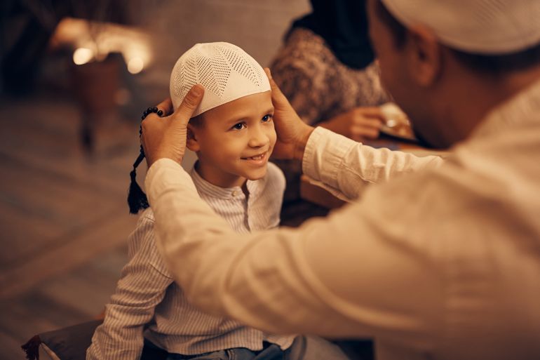 Close-up of Muslim father putting Kopiah hat on son's head at home. Focus is on kid.